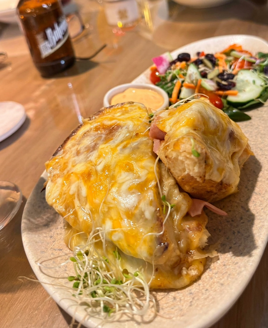 Sándwich gratinado con queso fundido, ensalada fresca y cerveza